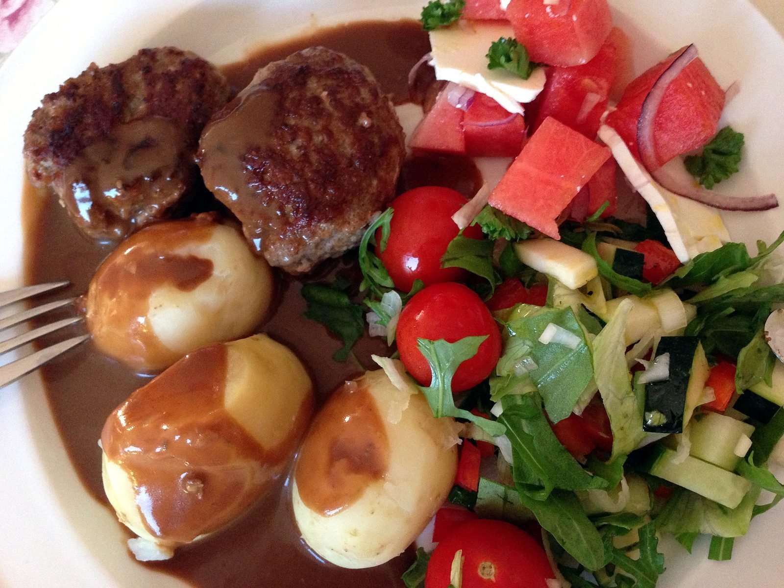 Frikadeller met aardappelen, bruine saus en een kleurrijke salade op een bord