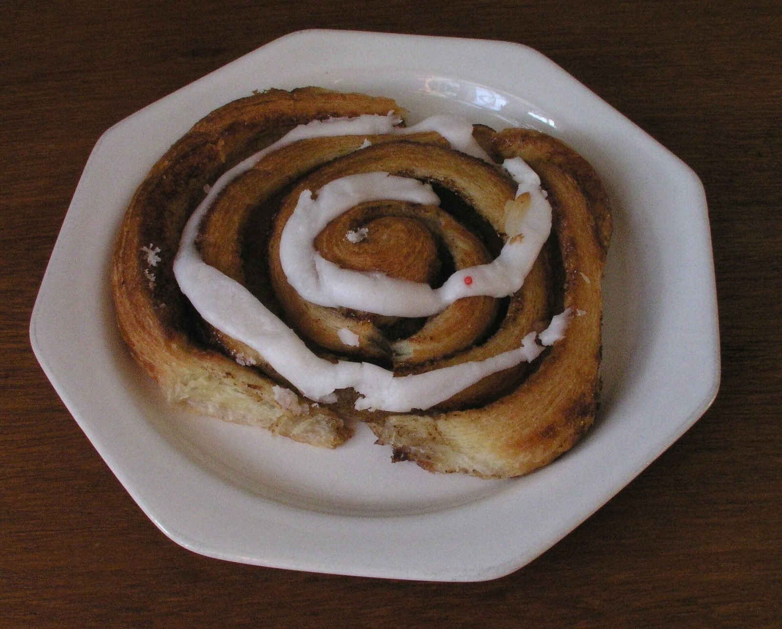 Deens kaneelbroodje met glazuur op een wit bord